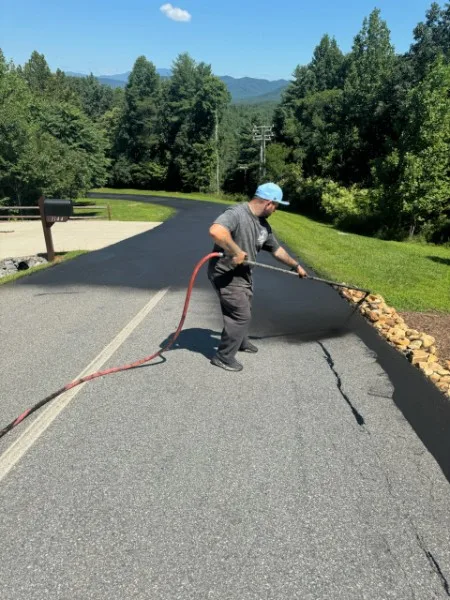 Tycoon Asphalt crew spraying fresh black sealcoat on a residential asphalt driveway with mountain views near Charlotte NC