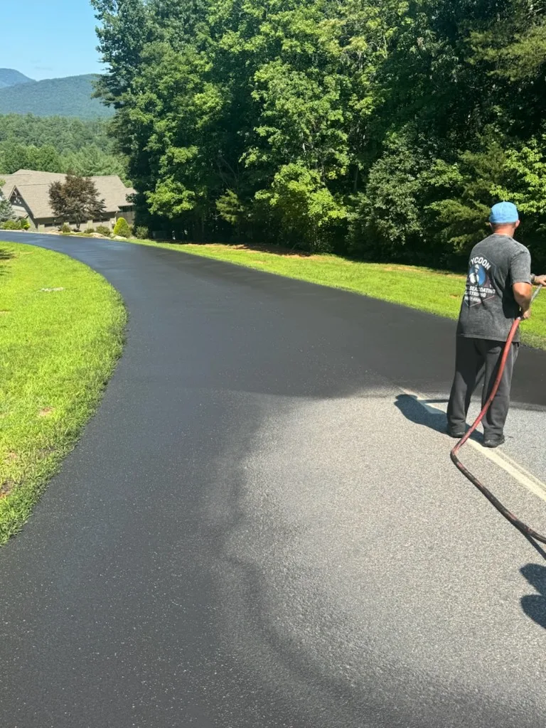 Tycoon Sealcoating & Striping crew applying jet-black sealer to a long curved residential driveway in Charlotte NC
